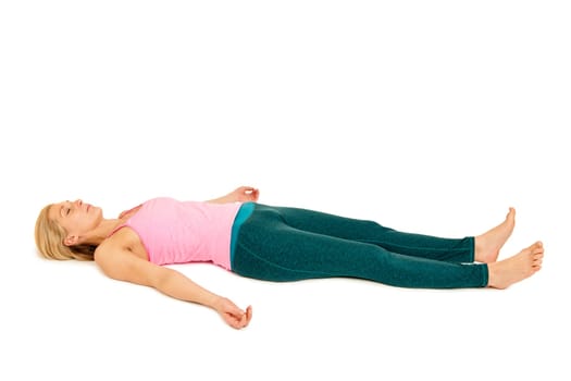 Flat-angled full-body side view of a young woman lying on her back in the yoga position "Totenstellung"" (shavasana) on a white background."
