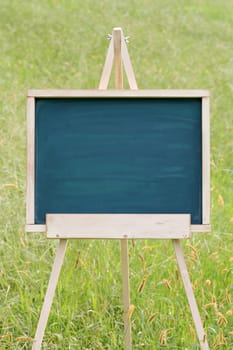 empty chalkboard with wooden easel on green field background