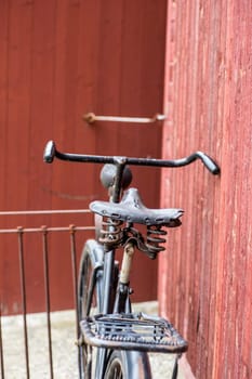 old retro antique black men's bicycle parked up of red wooden fence photographed from behind