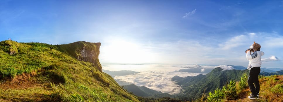 Panorama beautiful landscape nature of sunrise on peak mountain with sun cloud fog bright sky and woman tourist are taking photos in winter at Phu Chi Fa Forest Park, Chiang Rai Province, Thailand