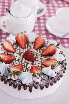 Tasty strawberry cream cake on checkered table, with tea set