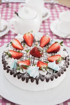 Tasty strawberry cream cake on checkered table, with tea set