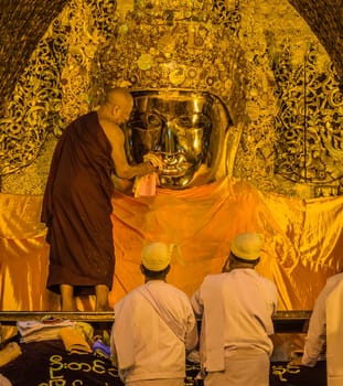 Early morning senior monk cleaning the teeth of Mahamuni Buddha in Mandalay, Myanmar