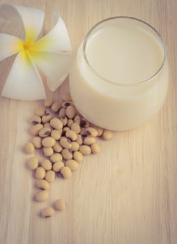 Fresh Soy milk (Soya milk) and dried soybean seeds on wooden background with white plumeria flower. Retro-Vintage filter effect