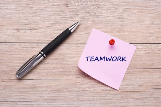 Word teamwork on pink sticky note and red pin and ballpoint pen