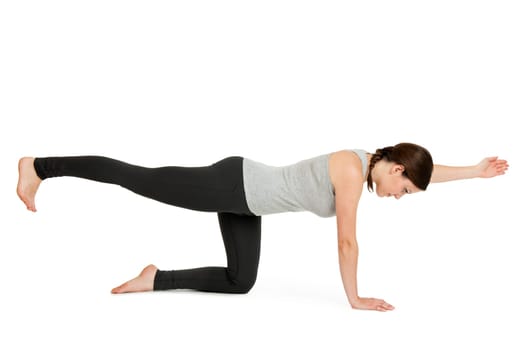 Lateral full-body view of a young woman against a white background showing the yoga exercise diagonal cat (Majariasana).