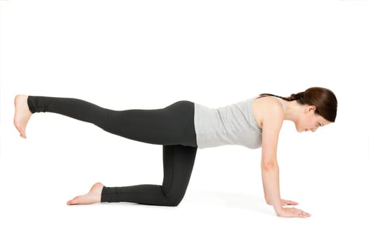 Lateral full-body view of a young woman against a white background showing the yoga exercise "cat"" (Majariasana)."