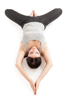 Elevated full-body view of a young woman lying on her back in the yoga position "lying butterfly"" (supta baddha konasana) on a white background."