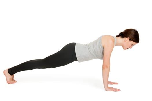 Lateral full-body view of a young woman against a white background showing the yoga exercise board position with stretched arms (chaturanga dandasana).