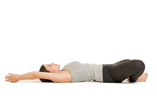 Lateral profile-full-body view of a young woman lying on her back in the yoga position "lying butterfly"" (supta baddha konasana) on a white background."