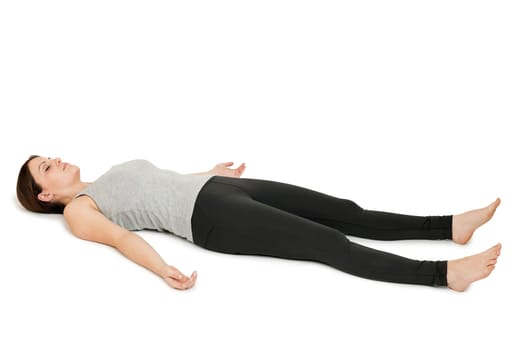 Flat-angled full-body view of a young woman lying on her back in the yoga position "Totenstellung"" (shavasana) on a white background."