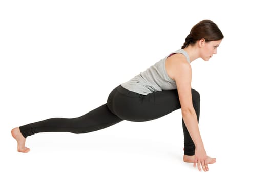 Lateral full-body view of a young woman against a white background showing the yoga exercise Lunge from the downward-facing dog (adho mukha svanasana).