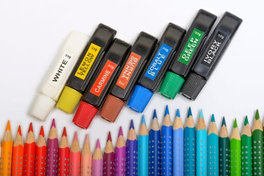 Bundle of colored pencils and tubes of paint on the colorful background