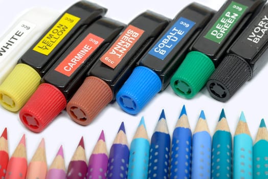 Bundle of colored pencils and tubes of paint on the colorful background