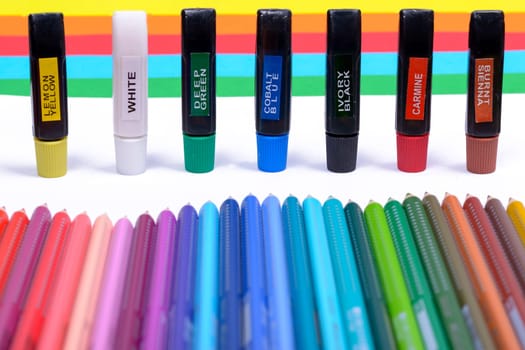 Bundle of colored pencils and tubes of paint on the colorful background