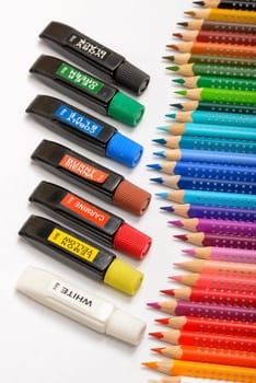 Bundle of colored pencils and tubes of paint on the colorful background