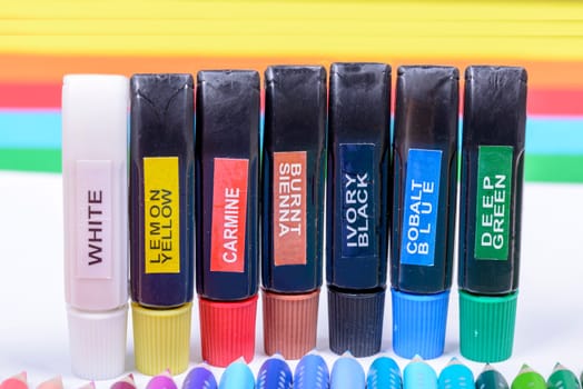 Bundle of colored pencils and tubes of paint on the colorful background