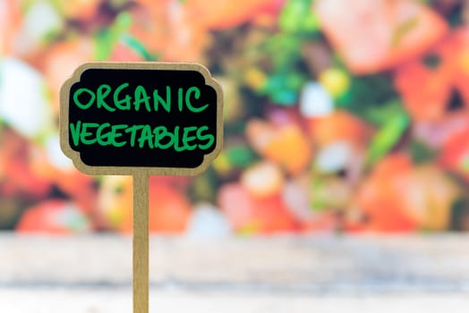 Wooden mini blackboard label over vegetable salad background and table with message ORGANIC VEGETABLES, copy space available