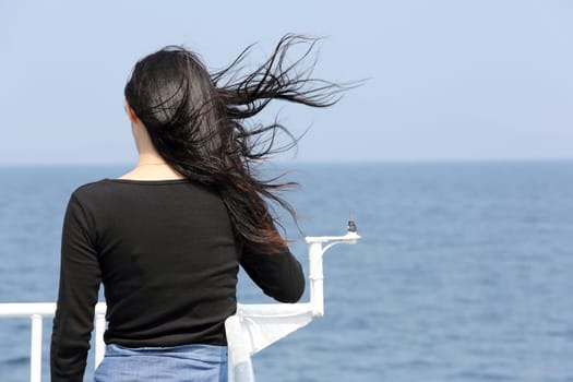 Back view of young asian woman with waving long hair from the deck of cruise ship