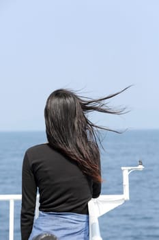 Back view of young asian woman with waving long hair from the deck of cruise ship