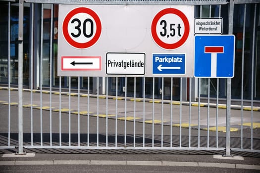 Many different traffic signs at the iron entrance gate of an industrial site.