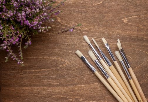 bunch of brushers and violet flower on brown wooden background