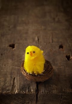 Cute little chicken decoration in a nest on a rustic wooden table, Easter or spring background
