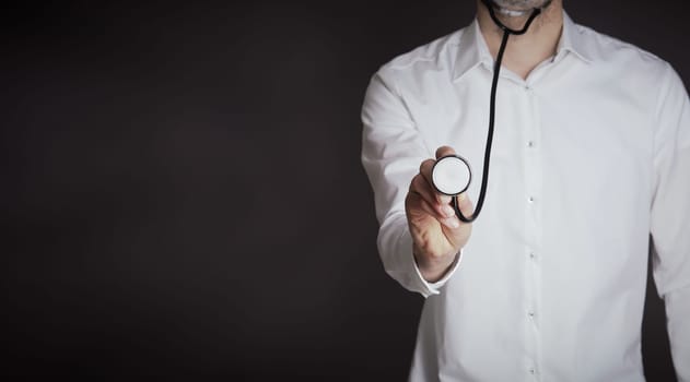Hand of a doctor with a stethoscope on a dark background with space for text or image, selective focus on foreground