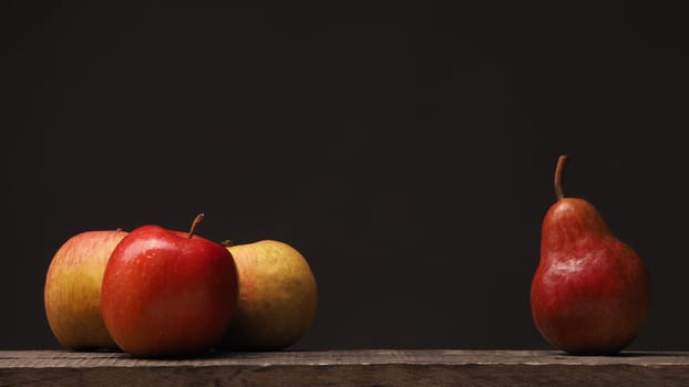 Three apples and one pear on a rustic wooden table, using as background with space for text