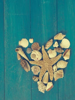 Heart shape of shells and a starfish on a blue vintage wooden background