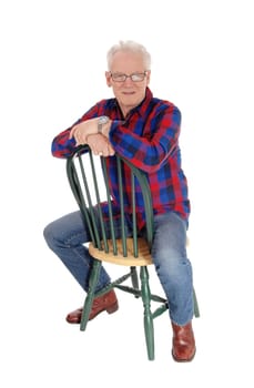 A handsome happy senior citizen sitting backwards on a green chair,.relaxing, isolated for white background..