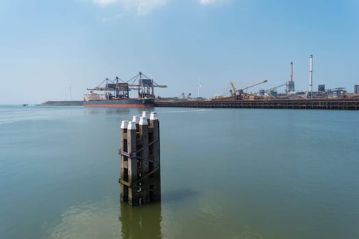 wooden poles that mark the waterway in front of a large steel plant