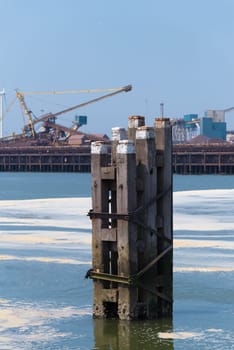 wooden poles that mark the waterway in front of a large steel plant