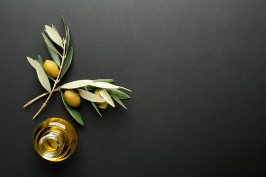 Olive oil and olive branch on black background