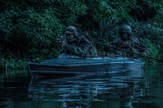 Special forces men with painted faces in camouflage uniforms paddling army kayak. Boat moving calmly across the river, diversionary mission, twilight