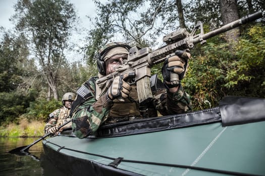 Special forces men with painted faces in camouflage uniforms paddling army kayak. Boat moving across the river, diversionary mission, front crop view