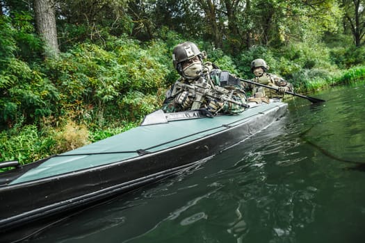 Special forces men with painted faces in camouflage uniforms paddling army kayak. Boat moving across the river, diversionary mission, diagonal view