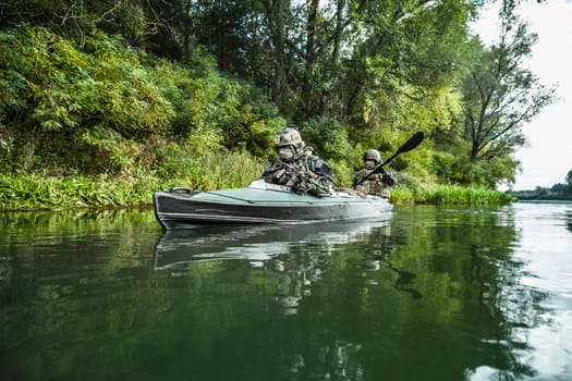 Special forces men with painted faces in camouflage uniforms paddling army kayak. Boat moving across the river, diversionary mission, diagonal view