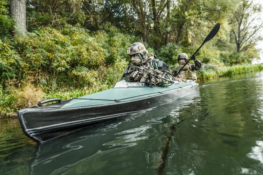 Special forces men with painted faces in camouflage uniforms paddling army kayak. Boat moving across the river, diversionary mission, diagonal view