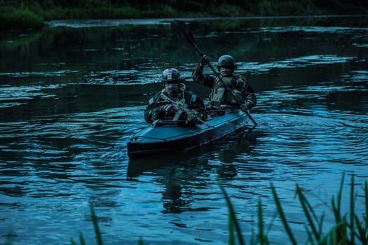 Special forces men with painted faces in camouflage uniforms paddling army kayak. Boat moving calmly across the river, diversionary mission, twilight