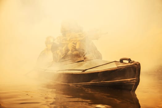 Special forces marine operators in camouflage uniforms paddling army kayak through river fog. Diversionary mission, machine gunner ahead