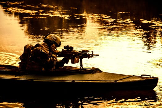 Special forces backlit machine gunner in army kayak. Boat moving calmly across the river, diversionary mission, sunset dusk