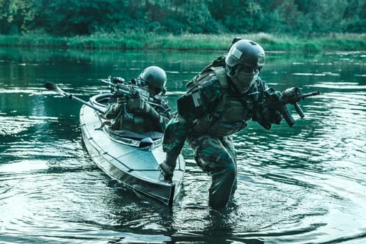 Covert landing. Pair of armed operators with painted faces disembarking from military kayak on river coast. Diversionary mission under cover of darkness