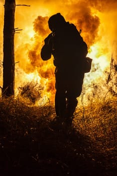 Backlit silhouette of special forces marine operator in forest on fire explosion background. Battle, bombs exploding, fighting no matter what