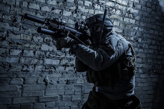 Special forces operator pointing weapon in the dark. Combat helmet, tactical radio system with folding antenna are on. Low key image