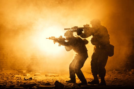 Black silhouettes of pair of soldiers in the smoke fire burning moving in battle operation. Back light
