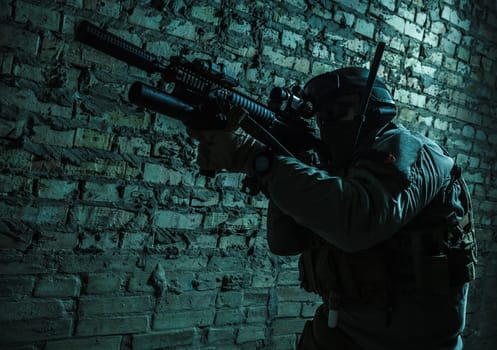 Special forces operator pointing weapon in the dark. Combat helmet, tactical radio system with folding antenna are on. Low key image