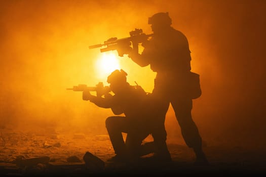 Black silhouettes of pair of soldiers in the smoke fire burning moving in battle operation. Back light