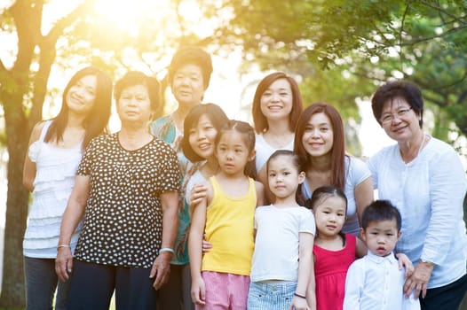 Large group of Asian multi generations family portrait, grandparent, parent and children, outdoor nature park in morning with sun flare.