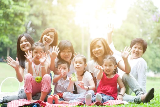 Group of Asian multi generations family portrait, grandparent, parents and children, outdoor nature park in morning with sun flare.